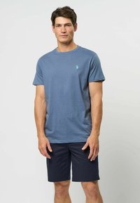 Niebieski bawełniany t-shirt z okrągłym dekoltem i krótkimi rękawami, z małym zielonym logo na piersi, w zestawie z ciemnoniebieskimi krótkimi spodenkami.