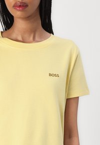 Tricou galben din bumbac, cu guler rotund și mâneci scurte, având un mic logo brodat "BOSS" în aur pe piept.