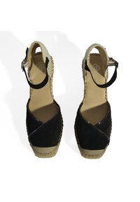 Chaussures espadrilles en suède noir avec une bride au niveau de la cheville, présentées avec un talon en jute tissé et un design entrecroisé avec des accents irisés.