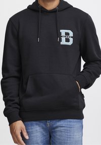 Sudadera negra de tela suave, cuenta con un bolsillo canguro en la parte frontal y una letra "B" decorativa en azul en el pecho. Capucha ajustable con cordón.