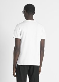 Camiseta blanca de algodón con un clásico escote redondo y mangas cortas, vista desde la parte posterior, combinada con pantalones negros.