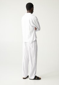 Hvid, løstsiddende skjorte og bukser lavet af letvægtsstof; kombineret med sorte sandaler; afslappet pasform med et casual design.