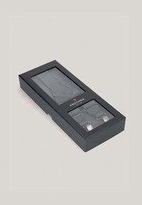 Szare szelki w czarnym pudełku, z wzorem w jodełkę, skórzanymi akcentami i srebrnymi metalowymi klipsami. Pudełko jest przezroczyste, co umożliwia podgląd zamkniętej zawartości.