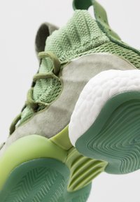 Zielony but sportowy z teksturowaną dzianinową cholewką, zamszowymi akcentami oraz białą gumową podeszwą z zielonymi detalami i wzorzystym bieżnikiem.