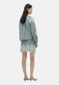 Top in lino azzurro chiaro con dettagli in pizzo sulle maniche; gonna mini coordinata con orlo in pizzo dettagliato e bordi ondulati; abbinata a tacchi color nocciola.