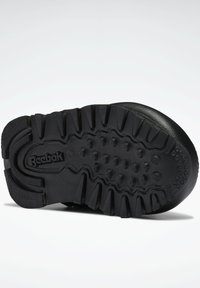 Svartgummi sko sula med texturerad yta, framträdande dobbar och cirkulära grepp. Har en präglad "Reebok" logotyp på sidan.