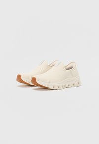 Slip-on tenisky v krémové pletenině s texturovanými vzory, s flexibilní bílou podrážkou a gumovými detaily v hnědé barvě.