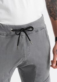 Grijze joggerbroek met een trekkoord in de taille, voorzien van zwarte accenten, een zachte textuur en zichtbare stikdetails.