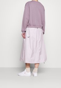 Lila sweatshirt med oversize-passform, kombinerad med en ljusrosa kjol i ankellängd som har en svart Nike-logotyp, samt vita sneakers.