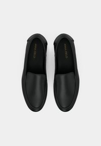 Black slip-on shoes with a smooth leather finish, round toe, elastic side panels, and a flat rubber sole. Gold branding inside.
