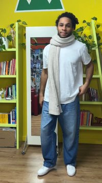 Kremowy dziergany szalik owinięty wokół torsu, w połączeniu z białym t-shirtem i luźnymi niebieskimi dżinsami, na tle jaskrawożółtego koloru.