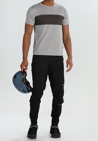 Camisa gris de manga corta con una franja marrón, pantalones negros y un casco azul. El atuendo presenta un diseño ajustado y un estilo deportivo.
