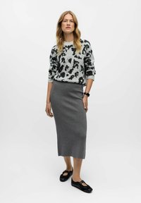 Pull en gris clair avec imprimé noir léopard, associé à une jupe grise ajustée et longue jusqu'à la cheville. Chaussures noires à enfiler. Tissu lisse et texturé.