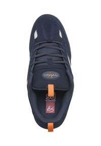 Marineblå semsket joggesko med mesh-detaljer, oransje snorholder, svarte lisser og gummisåle. Har logo på tungen og subtile syddetaljer.