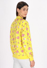Giacca bomber floreale gialla con un vivace stampa di fiori rosa e bianchi, colletto e polsini a costine, e una vestibilità rilassata.
