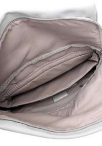 Intérieur d'un sac blanc avec un revêtement en tissu beige doux, comportant plusieurs compartiments, y compris une poche zippée et des coutures lisses.