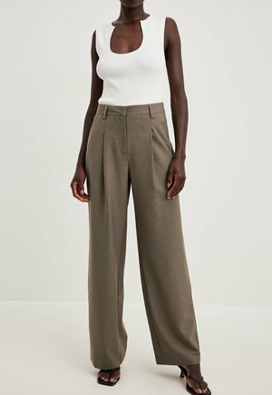 Model draagt een mouwloos wit geribbeld topje met een ronde hals en hoog getailleerde brede taupekleurige broek tegen een effen achtergrond.