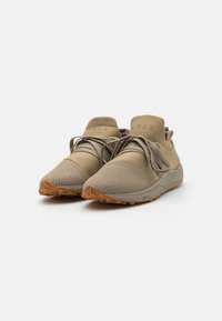 Beige sport sneakers met een gestructureerde geperforeerde voorkant, rubberen zolen, centrale elastische band en branding op de tong. Geaccentueerd met oranje details.