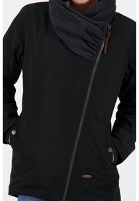 Mustat takki, jossa on vetoketjusuljetus, kauluksessa roikkuva harmaa huivi, sivutaskut ja brändätyt nahkaiset yksityiskohdat. Sujuva pinta.