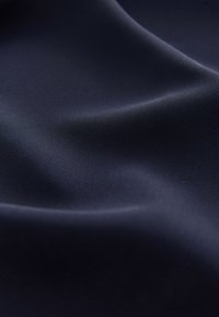 Tessuto blu scuro liscio con pieghe sottili e una fine trama diagonale a coste in una luce soffusa.