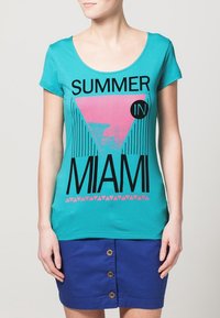 Camiseta de manga corta turquesa con un gráfico rosa que incluye el texto "VERANO EN MIAMI", complementada con una falda azul con detalles de botones.