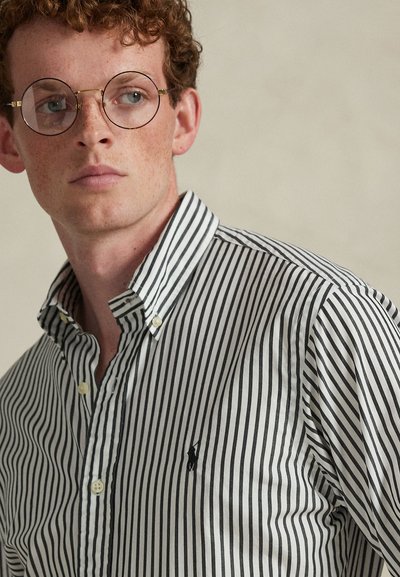 Ριγέ πουκάμισο με κάθετες μαύρες και λευκές ρίγες, σχέδιο με γιακά και μικρό λογότυπο στο αριστερό στήθος.