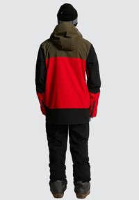 Veste de ski imperméable avec un design en blocs de couleur rouge, noir et olive, capuche ajustable et zips avant. Tissu durable et coupe décontractée.