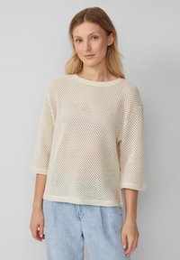 Maglione lavorato a maglia di un beige chiaro, con una vestibilità ampia e squadrata. Presenta maniche tre quarti, un collo rotondo e una texture in rete traspirante.