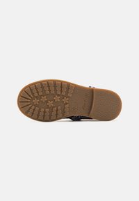 Sorte sandaler med glitrende stropper, gummisåle med teksturerte gripe mønstre, og en brun bunn med stjernesymboler. Størrelse 25.