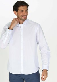 Chemise blanche à manches longues avec boutons, fabriquée dans un tissu lisse, dotée d'un col, d'une légère taille cintrée et de boutons sur le devant.