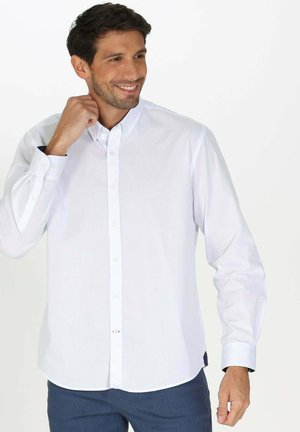 Chemise blanche à manches longues avec boutons, fabriquée dans un tissu lisse, dotée d'un col, d'une légère taille cintrée et de boutons sur le devant.