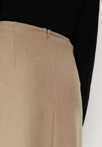 Beige wollen rok met een gladde textuur, voorzien van een discrete zijrits en strakke lijnen, gecombineerd met een zwart geribd topje.