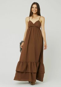 Robe maxi sans manches, marron, avec un décolleté en V, une taille froncée et un ourlet en volants superposés. Équipe de fines bretelles et d'une silhouette fluide.