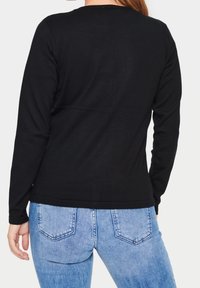 Schwarzes langärmliges Oberteil aus leichtem Stoff mit rundem Halsausschnitt, kombiniert mit hellblauen Jeans, die über Hintertaschen und ein abgewetztes Muster verfügen.
