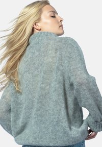 Jasnoszara, puszysta dzianinowa sweter z wysokim kołnierzem i luźnym krojem. Posiada ściągacze na mankietach i u dołu, eksponując miękką, teksturowaną powierzchnię.