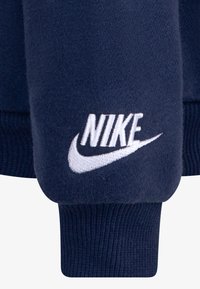Sudadera azul marino con puños y dobladillo de canalé. Presenta el logo de Nike bordado en blanco en la manga. Fabricada con un tejido suave y texturizado.
