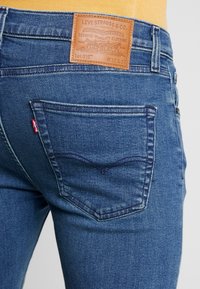 Jeans de denim azul con un corte clásico, que presentan una etiqueta de piel con la inscripción "Levi Strauss & Co." y bolsillos traseros con costuras distintivas.