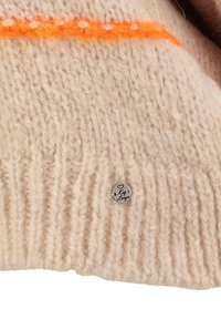 Tessuto di lana lavorato a maglia beige con motivo a coste, una striscia arancione vicino alla parte superiore e un piccolo etichetta metallica rotonda incisa con "Key Largo."