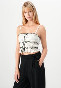 Top bianco corto con dettagli in ruffle neri e spalline sottili. Abbinato a pantaloni neri a vita alta con vita regolabile.