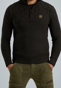 Pull vert foncé en tricot avec un col montant et une fermeture éclair, présentant un motif texturé en losanges sur la partie supérieure et un ourlet côtelé.