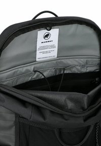 Interior de mochila Mammut negra que muestra el compartimento acolchado para laptop, un bolsillo con cremallera y una etiqueta con el logotipo de la marca y la declaración de misión.
