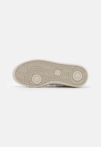 Suela de zapato con un patrón texturizado en espiga. Hecha de goma, con acentos circulares y un detalle de logo, en un color beige neutro.