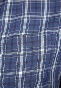 Camicia a quadri blu realizzata in tessuto leggero. Presenta strisce bianche e navy che si intersecano, e un dettaglio con tasca sul lato sinistro del petto.