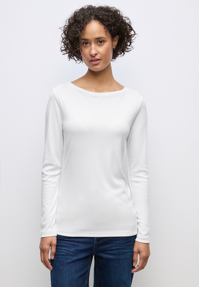 Weißes Langarmhemd mit weitem Ausschnitt und glatter Textur, kombiniert mit dunkelblauen Jeans. Einfaches, tailliertes Design.