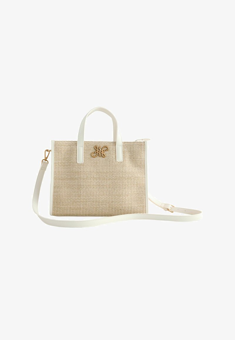 Sac à main en tissu beige avec poignées en cuir blanc, bordures et bandoulière réglable, ornée d'un logo décoratif doré sur le devant.