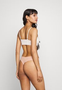 Bralette bianca senza cuciture con spalline regolabili abbinata a un perizoma a vita bassa di colore rosa pallido. Texture liscia con design minimalista, senza motivi.