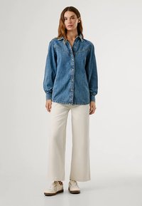 Denimskjorte med lange ærmer, lyseblå farve, knaplukning foran, to brystlommer, kombineret med cremefarvede bukser med vide ben og hvide sneakers.