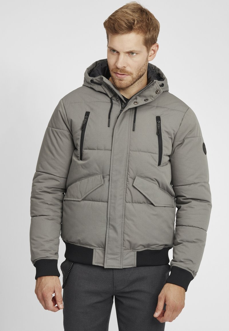 Veste doudoune grise avec capuche, dotée d'une poche zippée sur la poitrine, de poches latérales, de poignets côtelés et d'une texture de tissu durable.