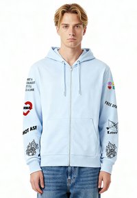 Felpa con cappuccio azzurro chiaro con zip, con testo e grafiche stampate sulle maniche. Tasca a marsupio frontale. Cappuccio con coulisse. Materiale in cotone, vestibilità comoda.