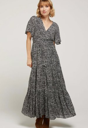 Robe maxi noire et blanche à motif paisley, avec des manches courtes et flottantes, un décolleté en V et un détail de jupe à volants, associée à des bottines brunes. 